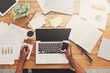 © Prostock-studio - Office workspace top view. African-american businessman working at wooden desk, using laptop and various objects all around