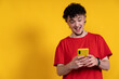 © Ceballos - Excited young man using smartphone on yellow background