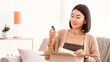 © Prostock-studio - Beauty Box Concept. Portrait of smiling asian woman received delivery package, holding foundation base for makeup, unpacking cardboard parcel with cosmetics product, sitting on the couch at home