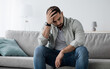 © Prostock-studio - Unhappy man touching hair, sitting on sofa at home, thinking about problems. Upset guy feeling lonely, sad, have psychological and mental troubles, suffering from bad relationship or break up