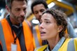 © Milos - A woman in a safety vest expresses concern while discussing an important issue with her colleagues in a warehouse setting, highlighting teamwork and communication.