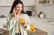 © Pixel-Shot - Young woman with sweet orange juice talking by phone in kitchen