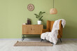 © Pixel-Shot - Brown armchair and chest of drawers near green wall in interior of room