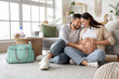 © Pixel-Shot - Happy pregnant couple sitting on carpet at home