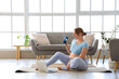 © Pixel-Shot - Sporty pregnant woman with water bottle and laptop sitting on yoga mat at home