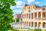 Visitors admire the grandeur of the Colosseum in Rome under a bright blue sky. The ancient structure showcases its majestic arches and historical significance to the city.