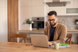 © Dorde - Bearded Man with Glasses Working on a Laptop at a Wooden Kitchen Table in a Bright, Modern Space