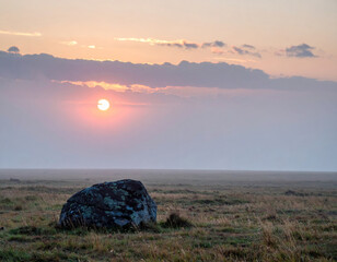 Wall Mural - solitary rock stands on misty plain as sun sets, casting warm glow across landscape. tranquil scene 