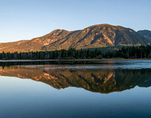 Wall Mural - serene mountain landscape reflecting in calm lake, surrounded by lush trees and clear sky, evokes sense of tranquility and natural beauty