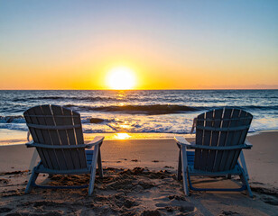 Wall Mural - Two beach chairs face ocean, creating serene atmosphere as sun sets on horizon, casting warm golden hues over tranquil waves