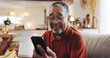 © peopleimages.com - App, phone and smile of senior man on sofa in living room of home for rest or retirement. Break, happy and social media with mature person reading text message in apartment for communication