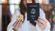© Sumala - Person holding passport and small wooden house model symbolizing international property ownership and travel opportunities with hope and confidence