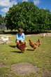 © Arianne - Young boy crouching and interacting with chickens in a farm setting