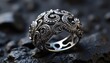 © Sanjula - Close up of an ornate silver ring with intricate designs and small stones on a textured dark surface