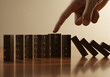 © Pixel Studio - A finger about to topple a line of dominoes demonstrates chain reaction consequences concept for business risk management and strategic planning success.