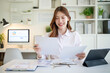 © wattana - Businesswoman smiling while reading reports at a clean, modern office desk.