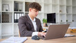 © wattana - Serious male entrepreneur reviewing notes and managing tasks online at a desk workspace.