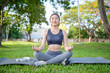 © wattana - Asian woman in activewear performing a serene meditation session surrounded by trees and open space.
