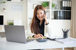 © wattana - Businesswoman talking on the phone while using a calculator at a modern office desk.