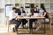 © saltdium - Group of young professionals having a business meeting in a modern office with laptops and reports, collaborating on a project around a wooden table