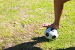 © Wavebreak Media - bare foot pressing soccer ball on patchy grass field under bright sunlight, casting sharp shadow