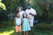 © Wavebreak Media - Laughing diverse family holding hands on sunlit garden lawn, with wooden bench background