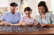 © New Africa - Happy parents and their daughter solving puzzle together at wooden table indoors