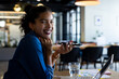 © WavebreakMediaMicro - Young adult African American woman sitting at table in open office, using speakerphone near laptop