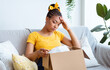 © Prostock-studio - Wrong Item Concept. Sad unpset african american lady sitting on couch and unpacking cardboard box, received parcel with damaged staff, feeling dissatisfied and disappointed with bad purchase