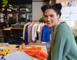© Wavebreak Media - Young woman smiling while sewing at indoor studio, using fabric rolls and tape, copy space