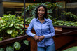 © Wavebreak Media - African American woman leaning on wooden planter in indoor atrium, showing plants and glass walls