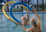 Smiling elderly man and woman exercising in water in evening