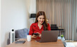 © David - The work of a remote employee online. Young confident asian woman works with laptop analyzes startup project strategy at workplace home office.