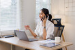 © David - Happy young business woman manager talking consulting client on cell phone working on laptop in the office. Busy woman professional business making call on cell using computer sitting at desk.