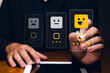 © Minttita - A person selects a happy face rating on a digital feedback interface, indicating positive customer satisfaction.