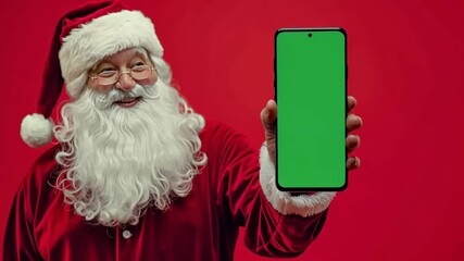 A festive santa claus cheerfully displays a smartphone with a bright green chroma key screen. The vibrant red background enhances the holiday spirit, making it suitable for christmas-themed projects.