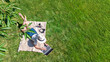 © Iuliia Sokolovska - Young woman using laptop computer in park, student girl freelancer working and studying online outdoors sitting on grass with headphones and laptop, aerial drone view from above