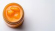 © Light of Art - An overhead shot shows a clear glass jar filled with smooth, bright orange baby food sitting on a pristine white surface in a brightly lit studio setting.