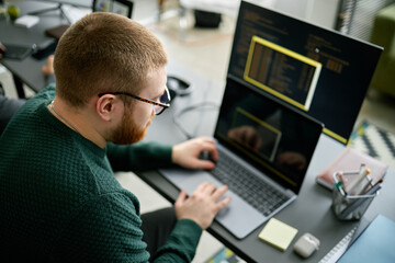 Coder working on project with two monitors and a laptop, immersed in code. Office environment showing programmer focused on software development