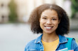 © Anastasiya - Closeup Portrait Of Cheerful African American female student wearing a denim jacket, smiling black female holding books and backpack, standing confidently in front of university building, free space