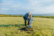 © Alexandr - Grandfather and Granddaughter Planting Tree in Scenic Countryside