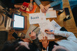 © qunica.com - A team of individuals engaged in a collaborative discussion involving paperwork, graphs, and digital technology to strategize and succeed in their work goals.