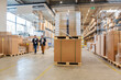 © Westend61 - Employees meeting in a large warehouse with stacked pallets and boxes