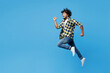 © ViDi Studio - Full body side profile view young happy Indian man he wear yellow checkered shirt casual clothes jump high do winner gesture isolated on plain blue cyan background studio portrait. Lifestyle concept.