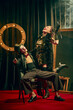 © master1305 - Expressive laughter and dramatic poses of two cabaret performers in vintage costumes on confetti-covered red carpet with smoke, lively moment. Concept of cabaret, show, circus, retro, vintage