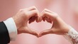 © khumthong - A Couple's Hands Forming a Heart Shape Symbolizing Love and Romance on a Pink Background