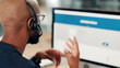 © FremtonClay/peopleimages.com - Black man, screen or consultant with computer at call center for online advice, help or customer service. Back, chat or sales agent with headset for virtual assistance, contact support or feedback