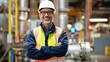 © Kowit - A middle-aged male engineer wearing safety gear smiles confidently in an industrial facility setting.