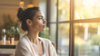 © Kowit - A young woman sits indoors, gazing thoughtfully out a sunlit window, surrounded by a calm and cozy atmosphere.