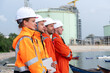 © Freeday photo - Group of workers in safety gear observing operations at industrial site near water in daytime
